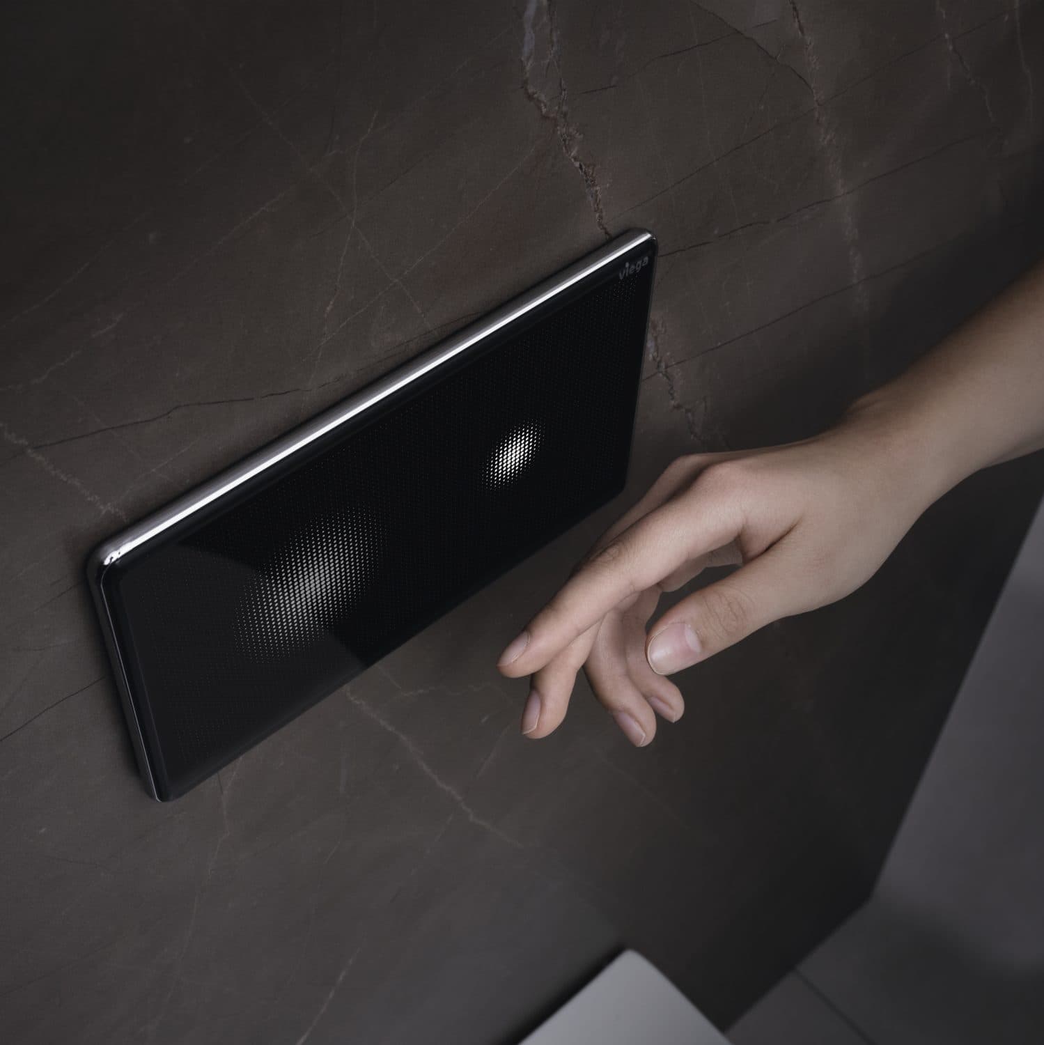Hand operating a black Viega flush plate on a dark wall